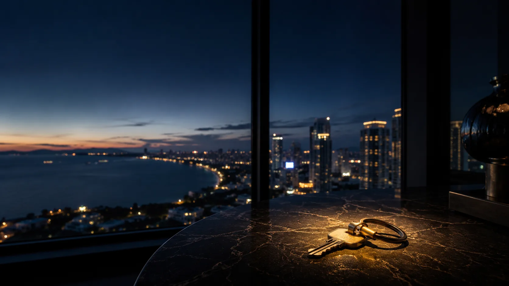Wohnungsschlüssel auf einem Tisch, dahinter die Skyline von Pattaya am Abend