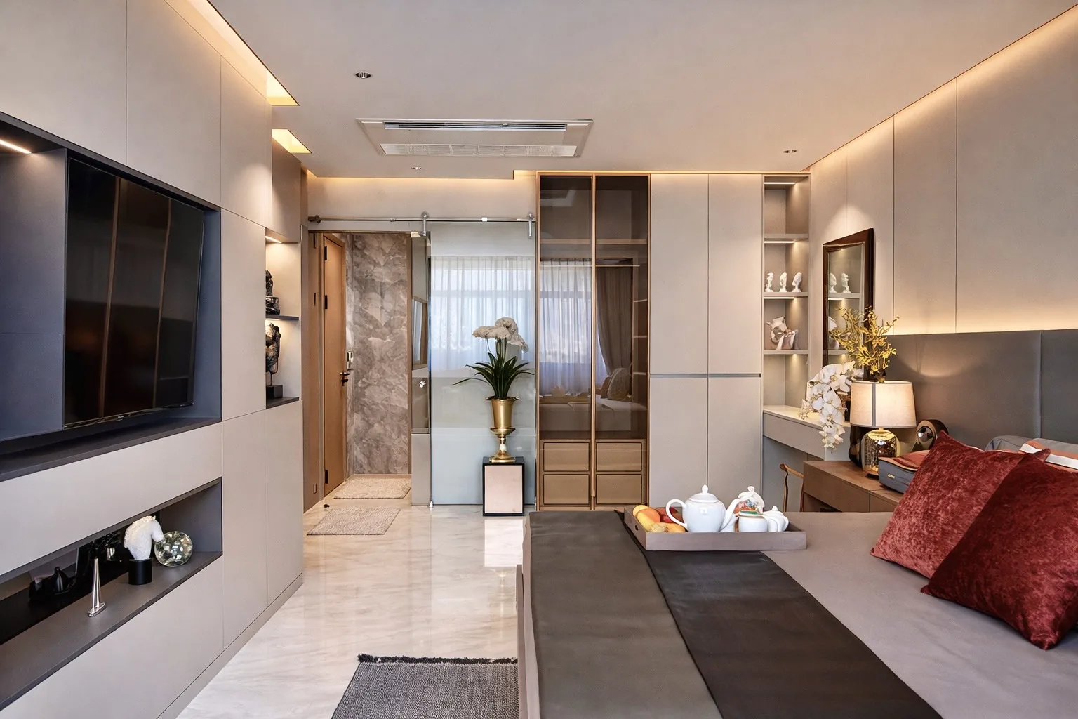 Modern eingerichteter Wohn- und Schlafbereich einer Musterwohnung im Sea Sky by Sands in Pattaya, mit wandmontiertem TV, Medienwand, Ankleidebereich und Bett mit roten Samtkissen