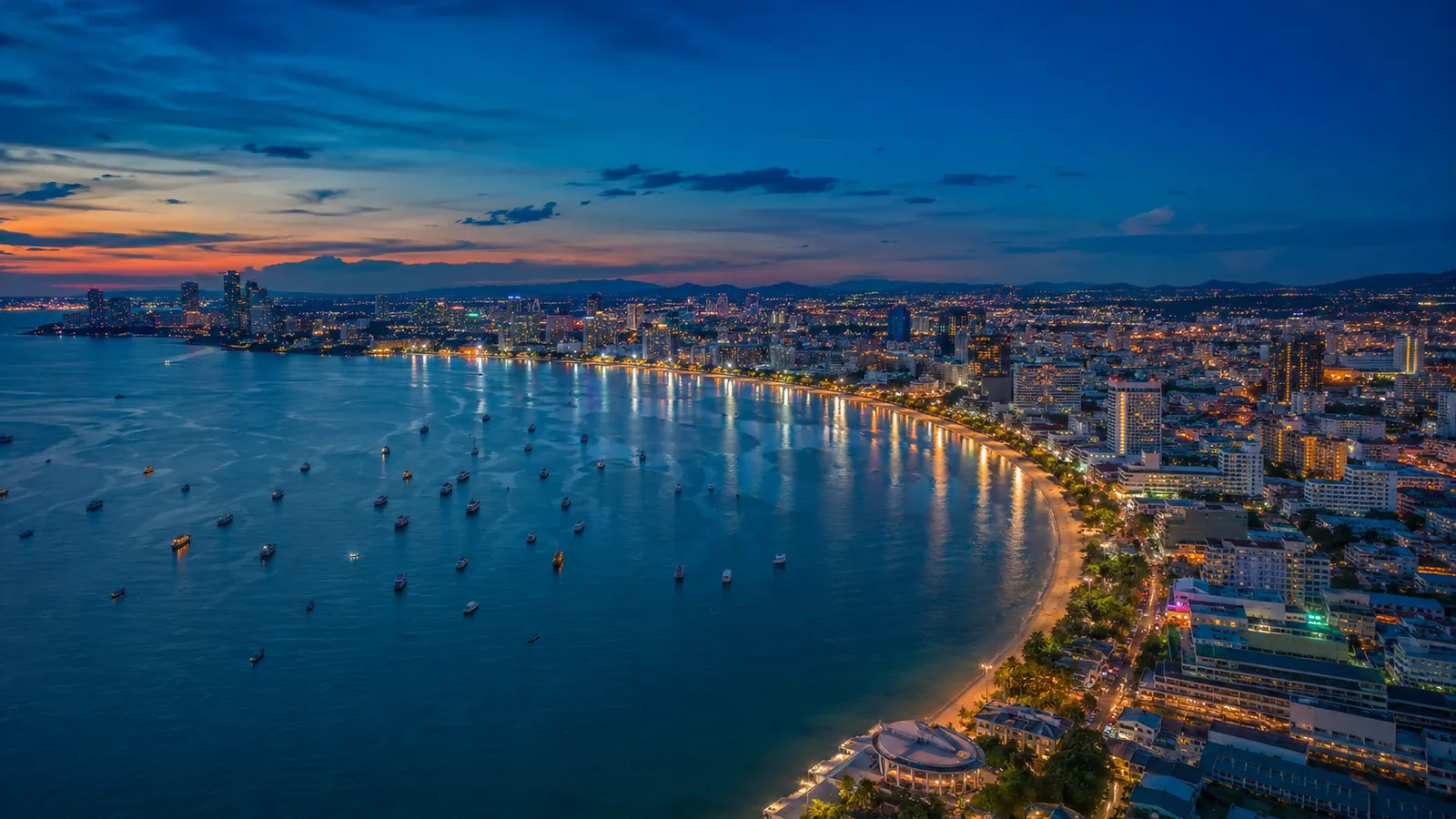 Luftaufnahme der gesamten Pattaya-Bucht am Abend mit leuchtender Stadt (Symbolbild, KI-generiert)